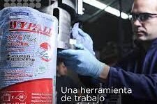 Una persona con guantes opera maquinaria junto a una pila de toallitas WypAll X75-60 multirag. El texto en español dice: Una herramienta de trabajo confiable, ¡siempre!.