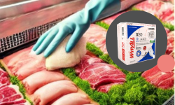 Una mano con un guante azul limpia cuidadosamente una vitrina de carne llena de carne y verduras envasadas, asegurándose de que estén limpias y presentadas. La imagen insertada revela una caja de guantes desechables etiquetados en coreano. La escena resalta sutilmente el uso adecuado de los productos WypAll duraderos para prácticas de higiene.